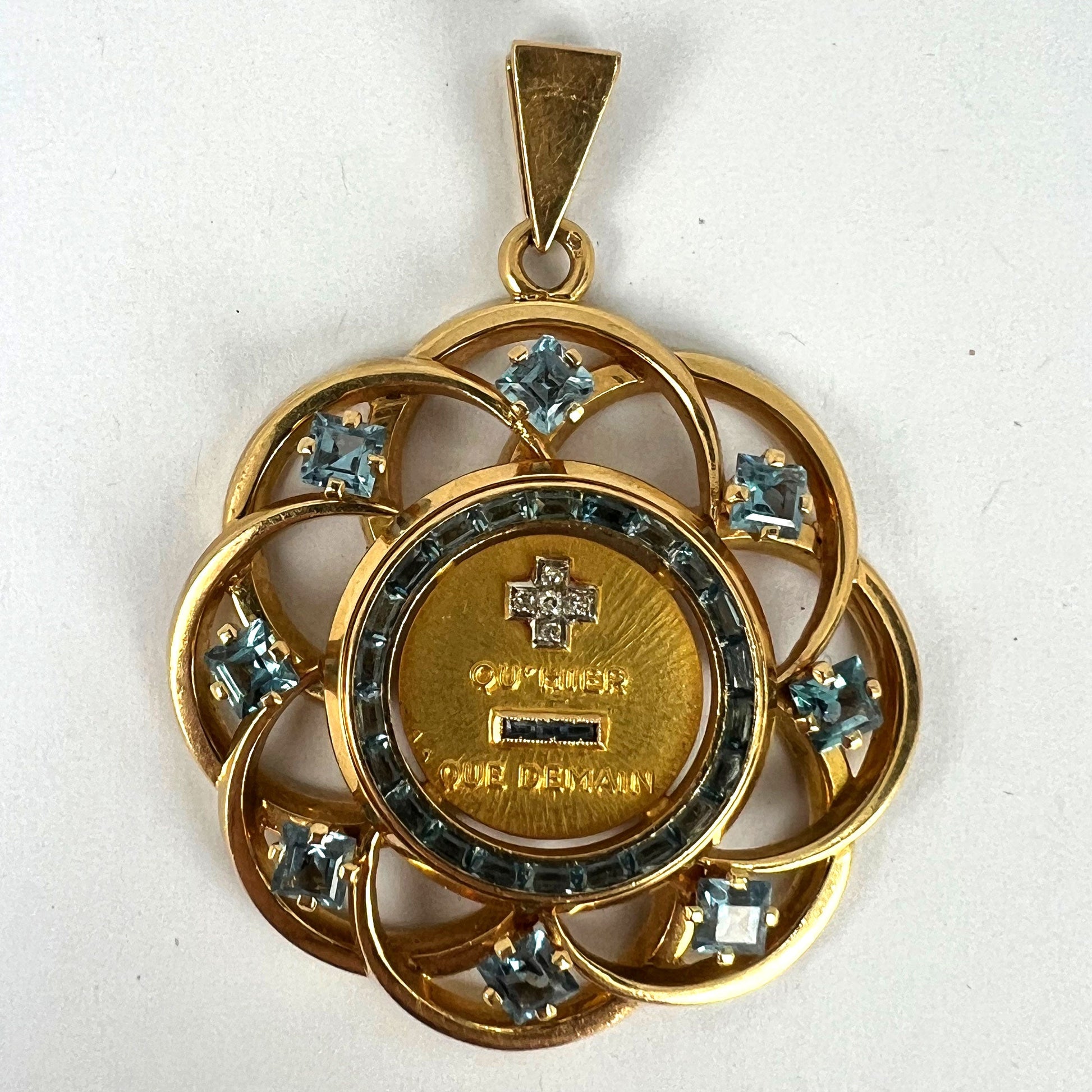 A yellow gold French QU'HIER QUE DEMAIN pendant with blue stones and diamonds, on a white background