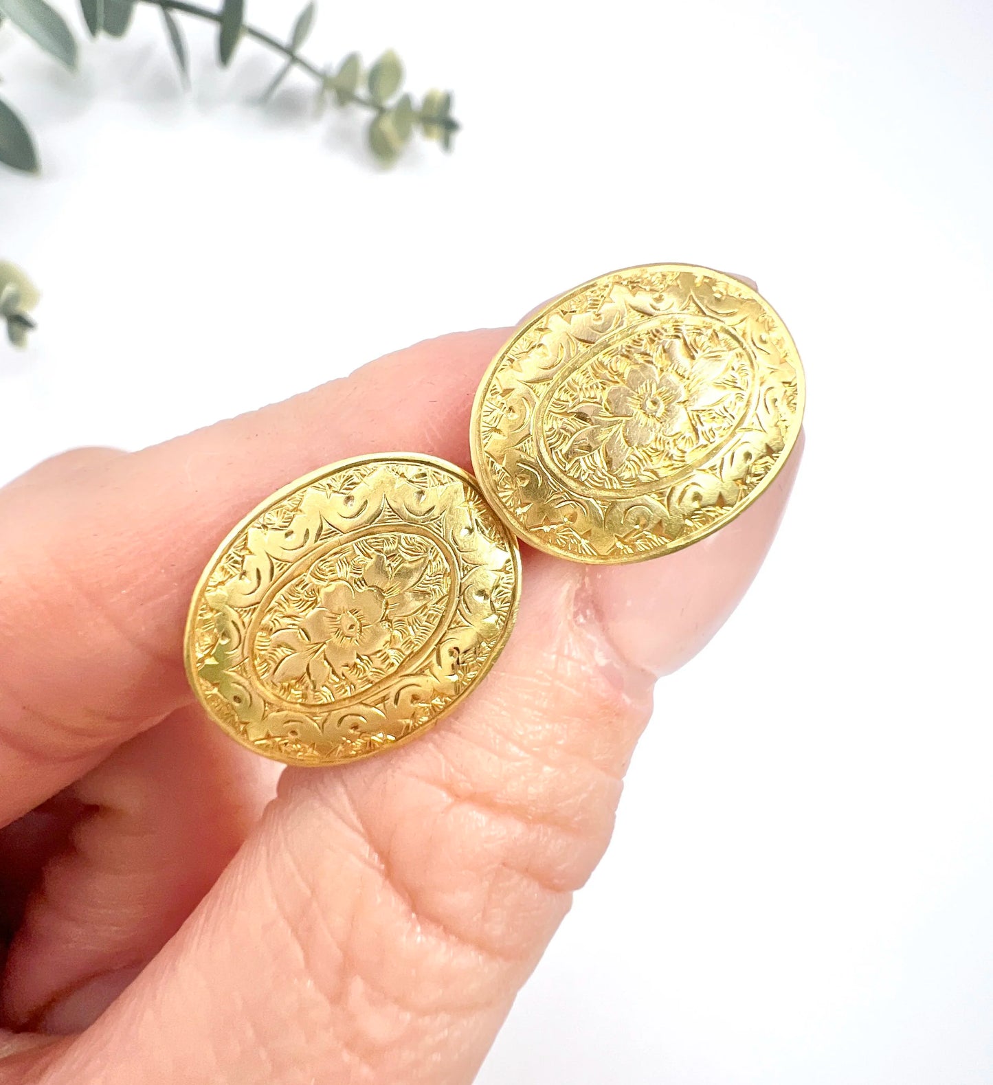A pair of yellow gold oval engraved cufflinks, held in a hand