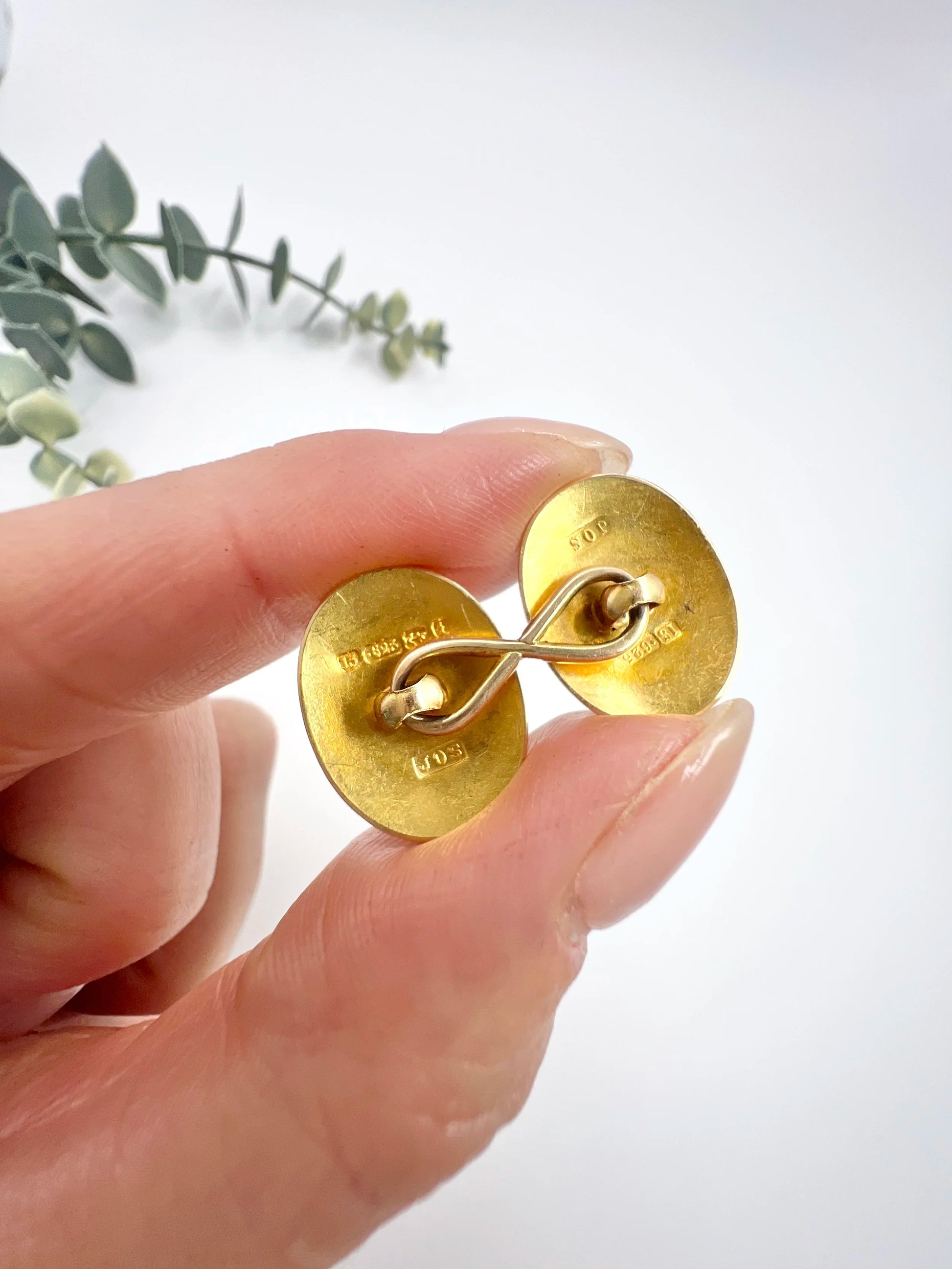 The back of a yellow gold cufflink, held in a hand