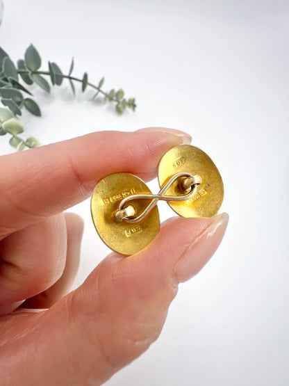 The back of a yellow gold cufflink, held in a hand