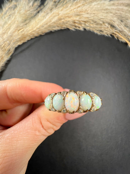 A cabochon opal and diamond carved half hoop ring in yellow gold, held in a hand