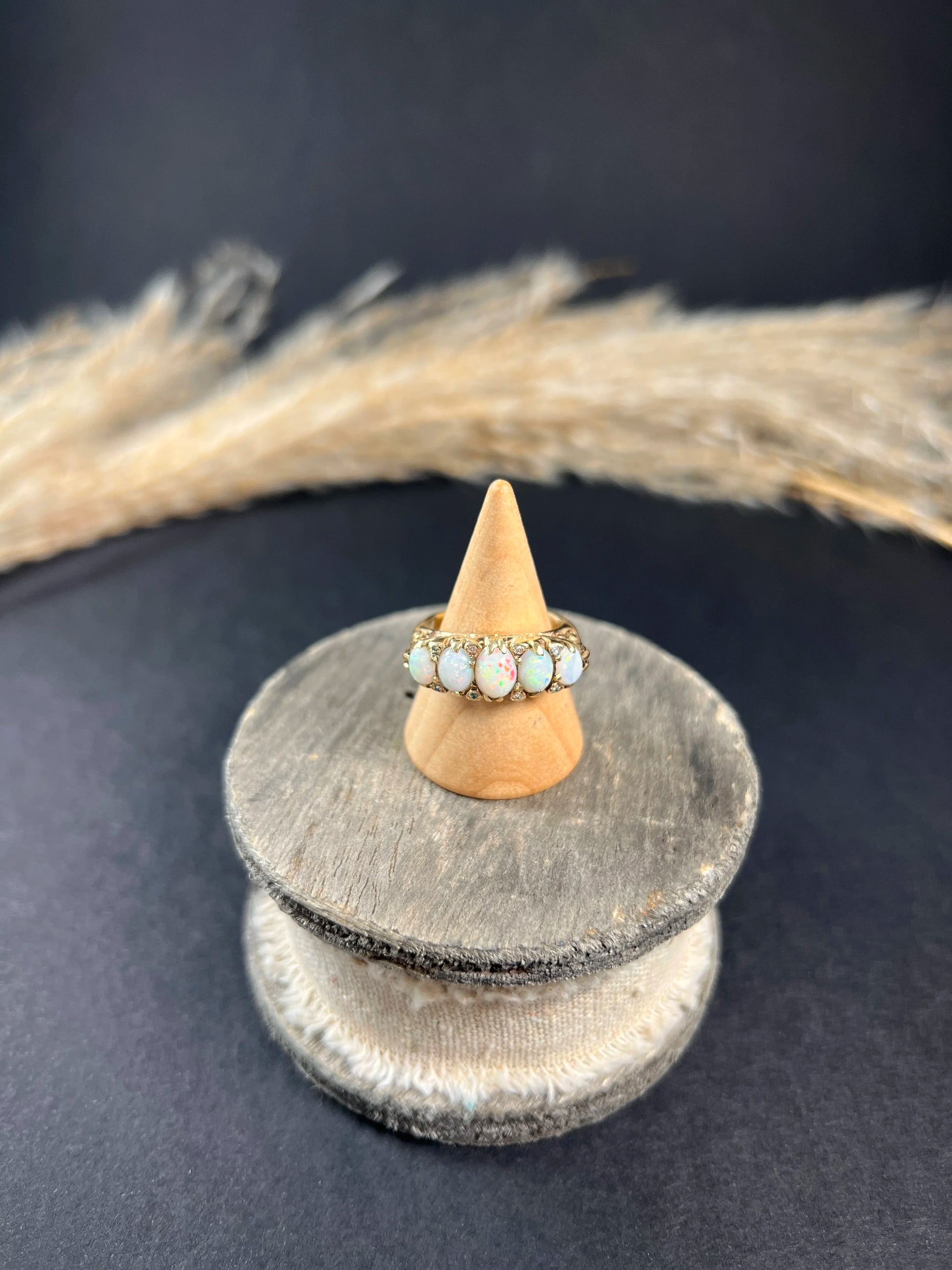 A cabochon opal and diamond carved half hoop ring in yellow gold, on a wooden ring cone