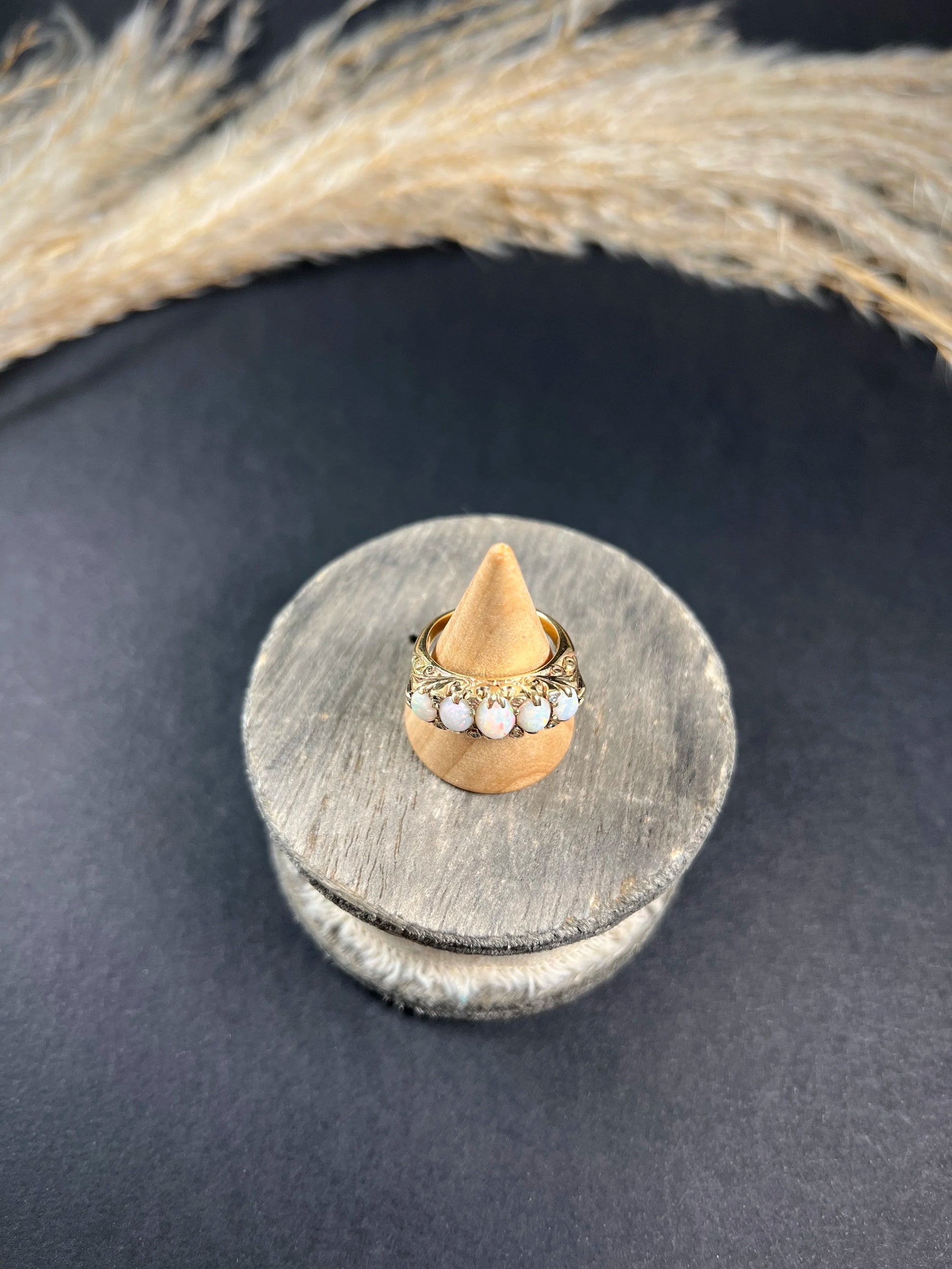 A cabochon opal and diamond carved half hoop ring in yellow gold, on a ring cone