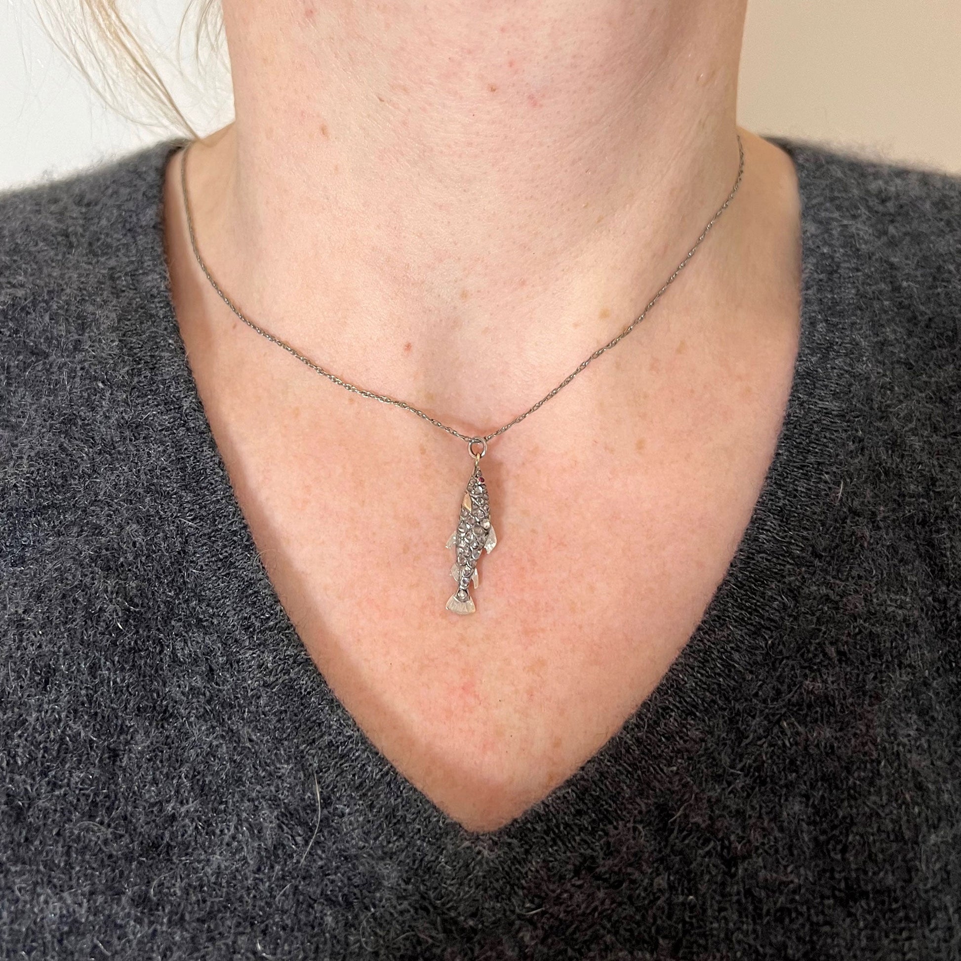 A fish shaped pendant with rose cut diamonds and ruby eye, on a white background modelled with a white metal chain