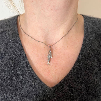 A fish shaped pendant with rose cut diamonds and ruby eye, on a white background modelled with a white metal chain