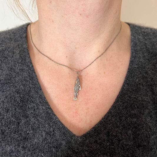 A fish shaped pendant with rose cut diamonds and ruby eye, on a white background modelled with a white metal chain