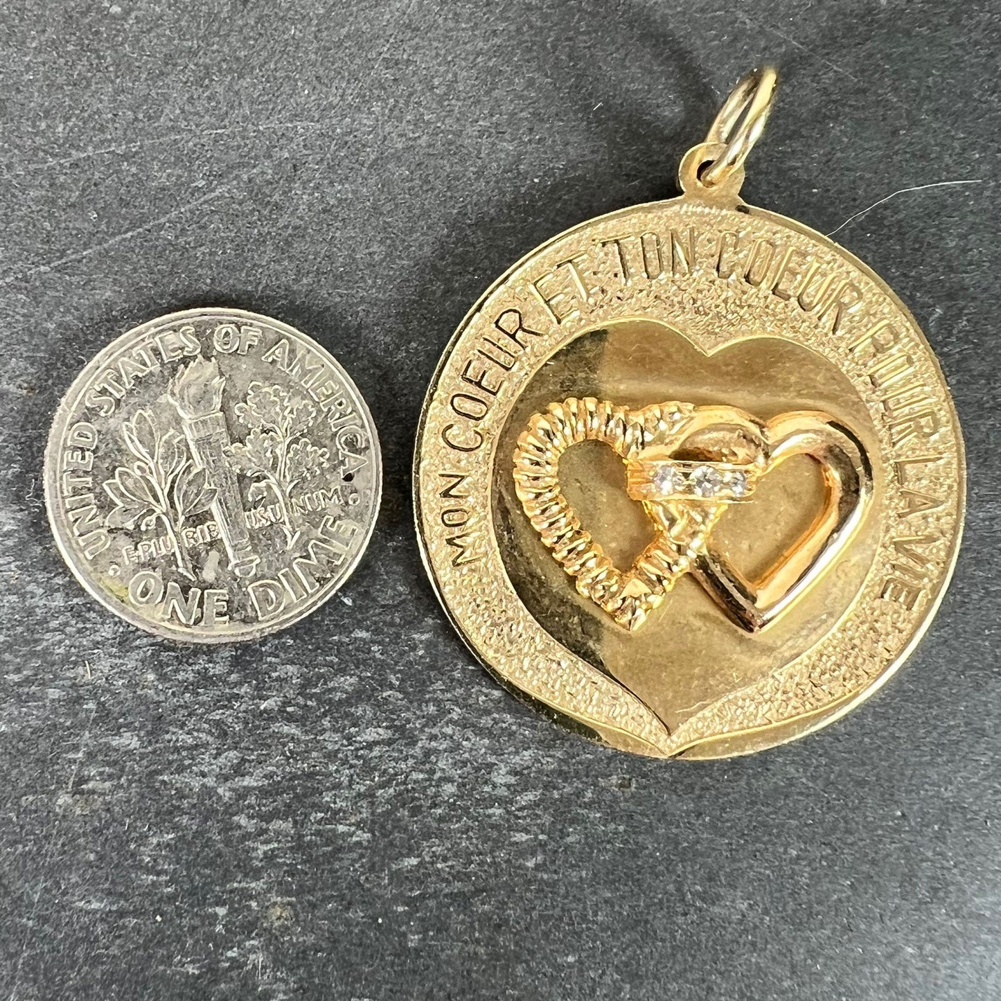 A round yellow gold love heart diamond pendant engraved MON COEUR ET TON COEUR POUR LA VIE, next to a dime coin