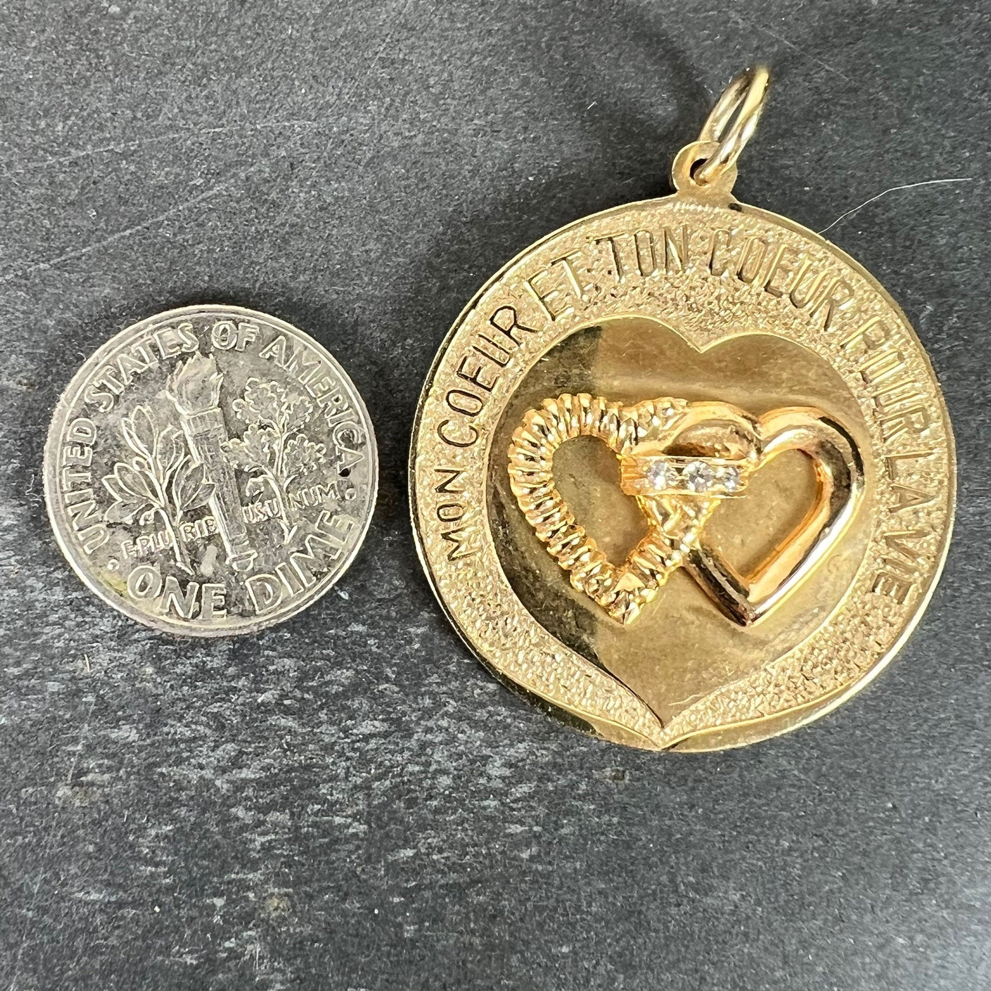 A round yellow gold love heart diamond pendant engraved MON COEUR ET TON COEUR POUR LA VIE, next to a dime coin
