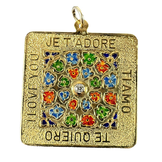 A square shaped yellow gold pendant with enamelled flowers and a central diamond, with text reading JE T'ADORE, TI AMO, TE QUIERO, I LOVE YOU