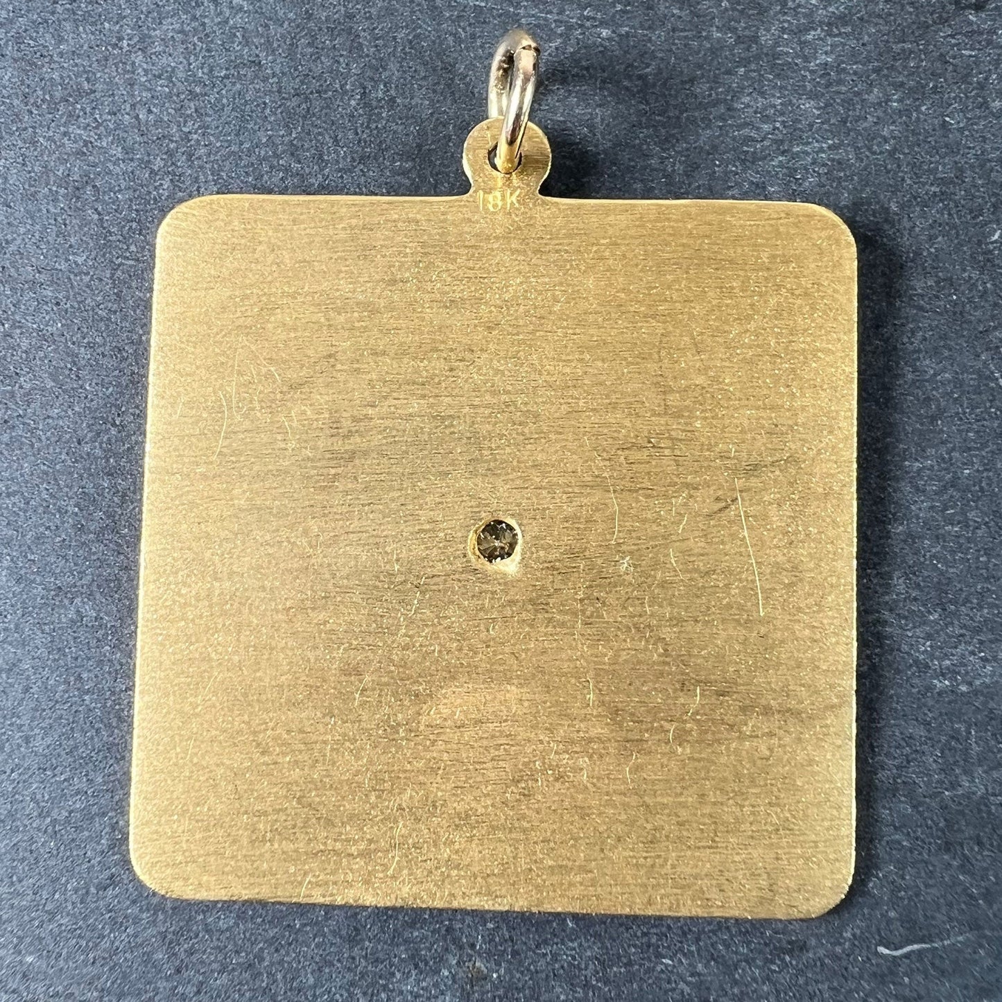 A square shaped yellow gold pendant on a grey background