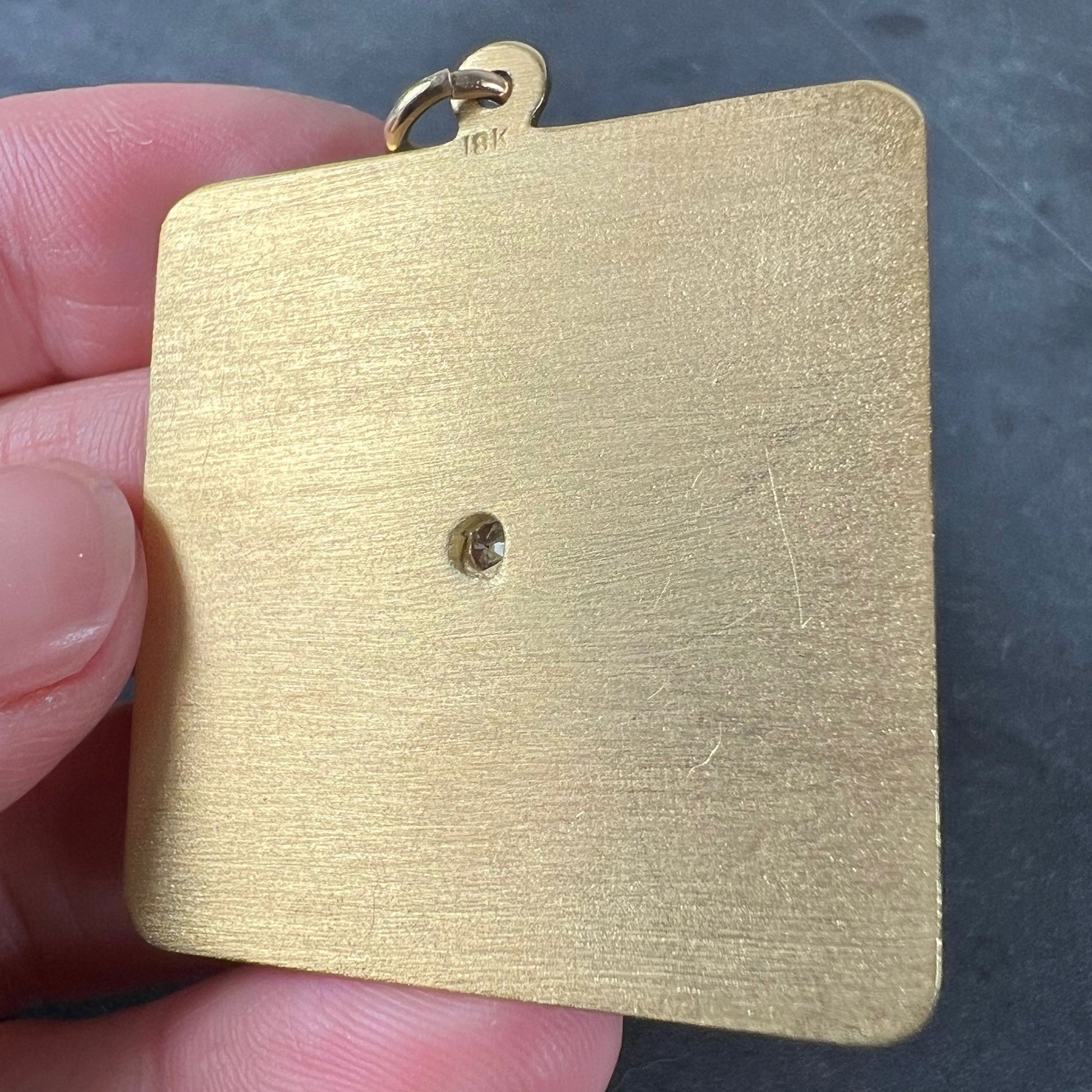 A square shaped yellow gold pendant held in a hand