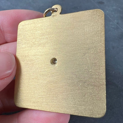 A square shaped yellow gold pendant held in a hand