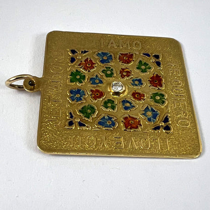 A square shaped yellow gold pendant with enamelled flowers and a central diamond, with text reading JE T'ADORE, TI AMO, TE QUIERO, I LOVE YOU