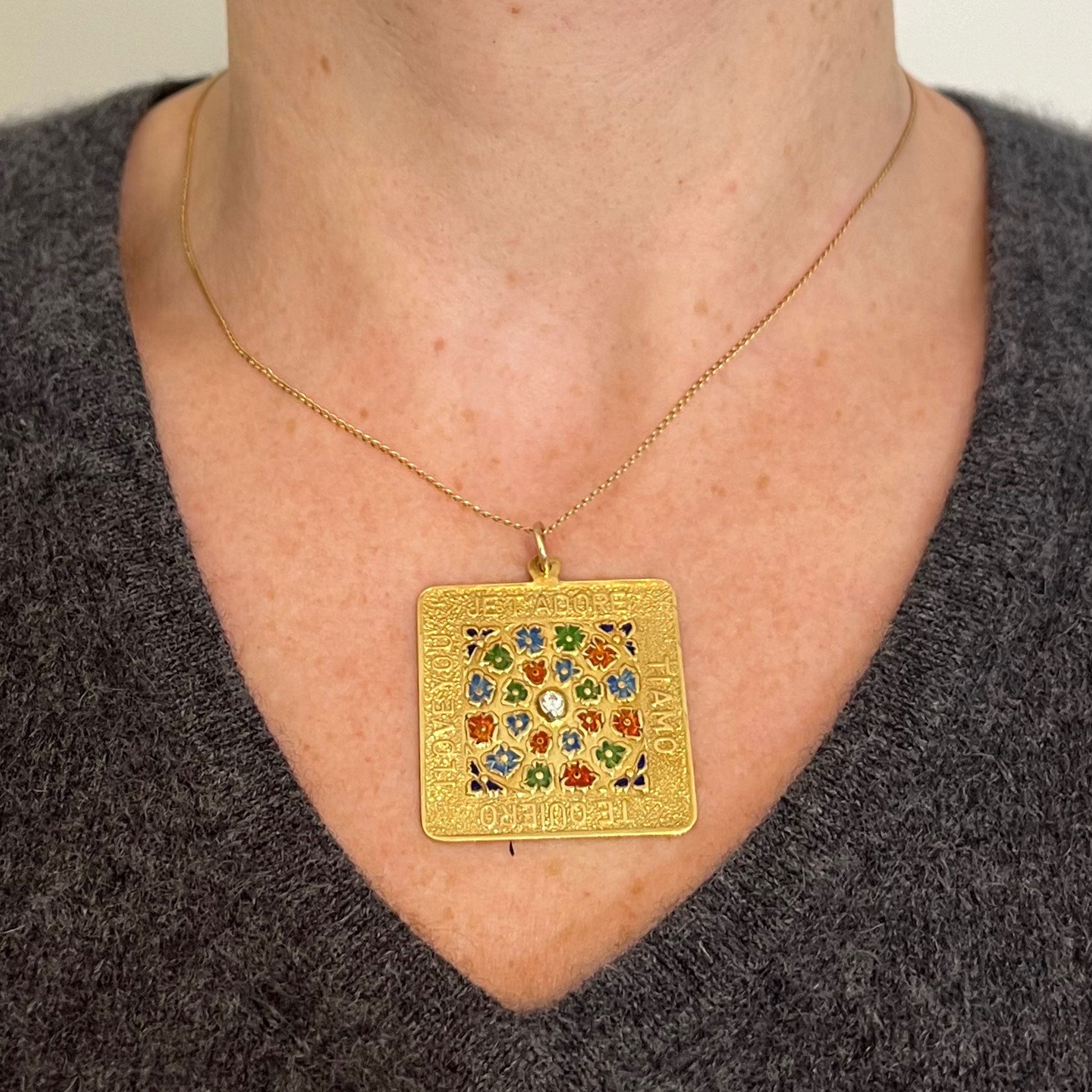 A square shaped yellow gold pendant with enamelled flowers and a central diamond, with text reading JE T'ADORE, TI AMO, TE QUIERO, I LOVE YOU, modelled on a gold chain