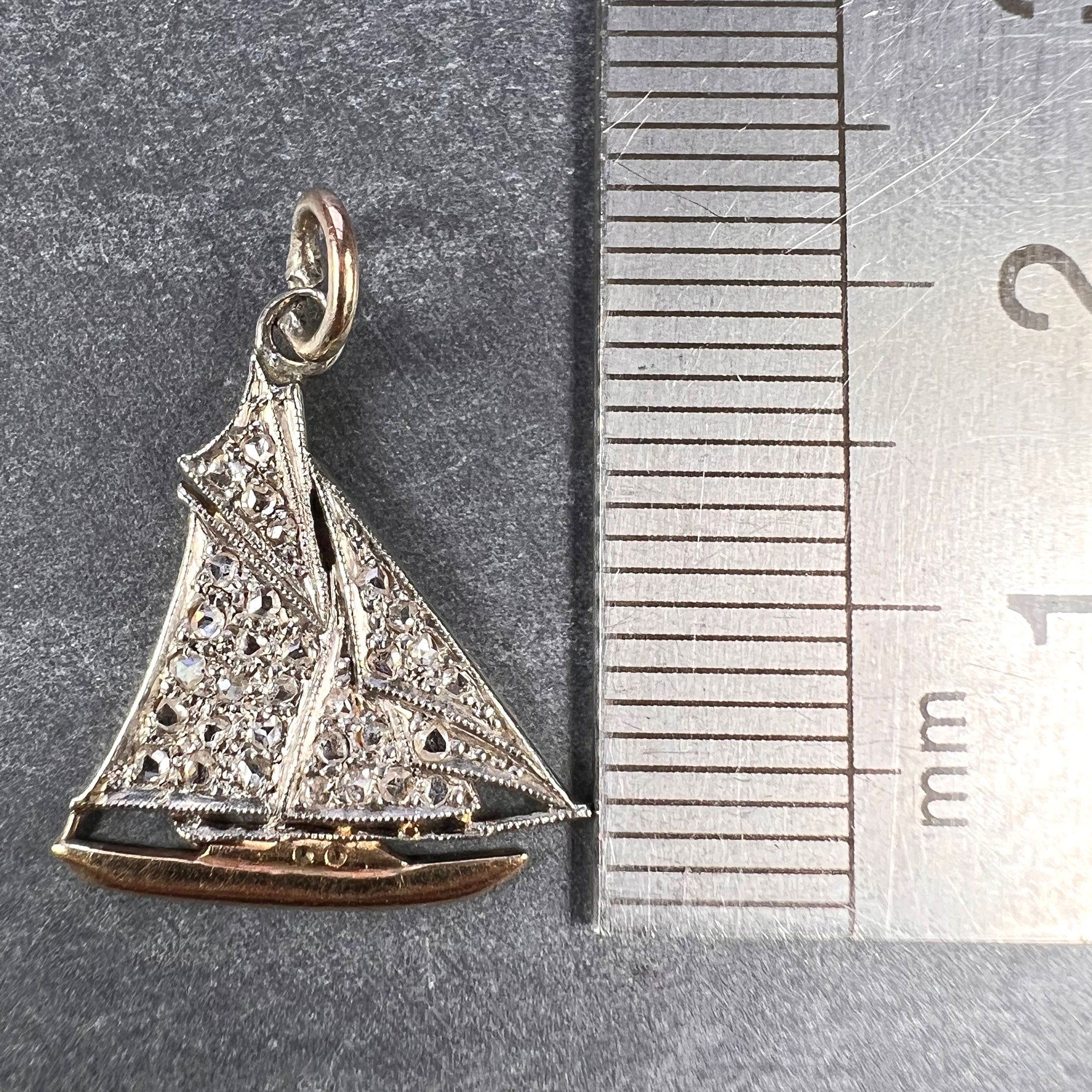 A diamond set yacht boat pendant, next to a metal ruler on a grey background