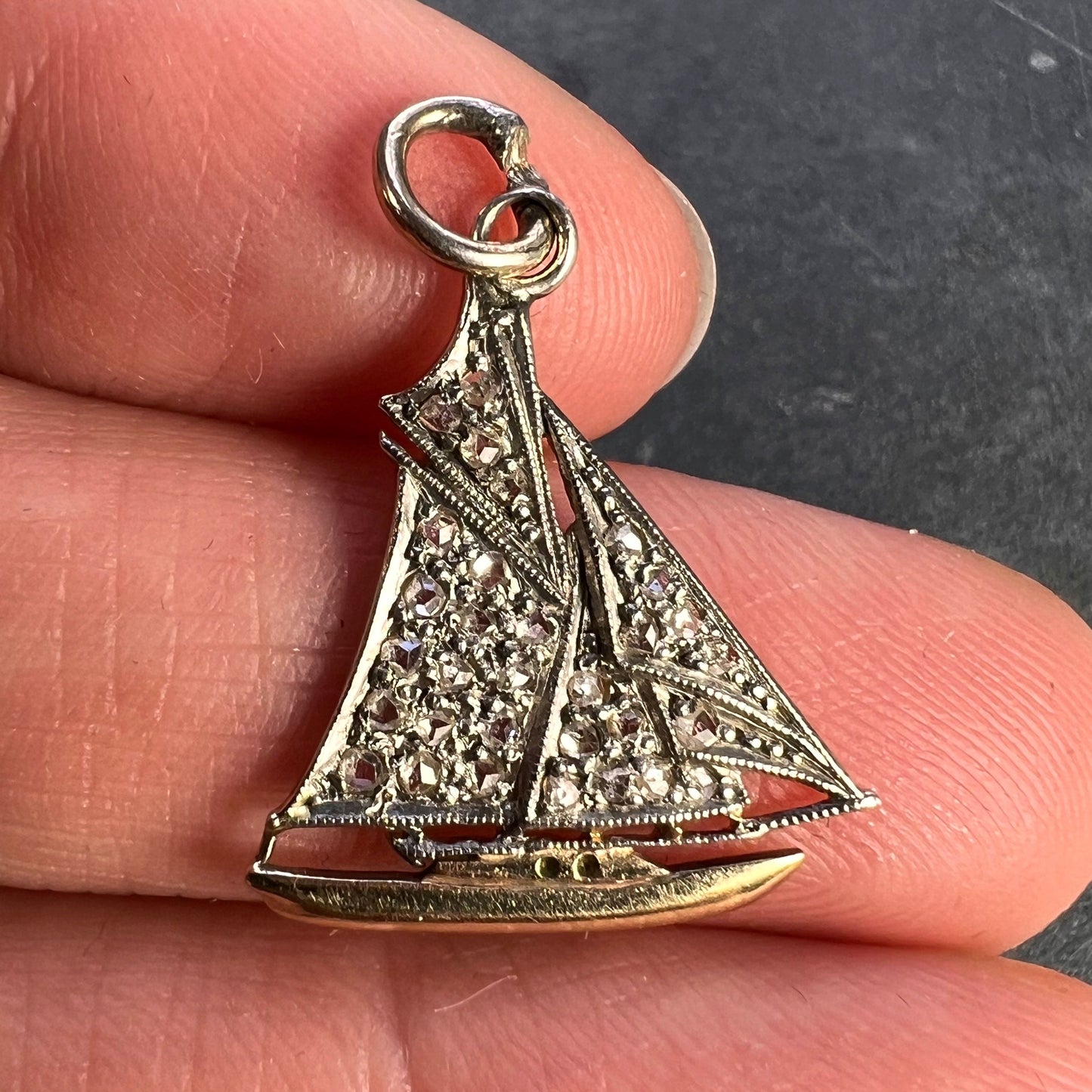A diamond set yacht boat pendant, held in a hand on a grey background