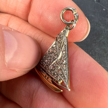 A diamond set yacht boat pendant, held in a hand on a grey background