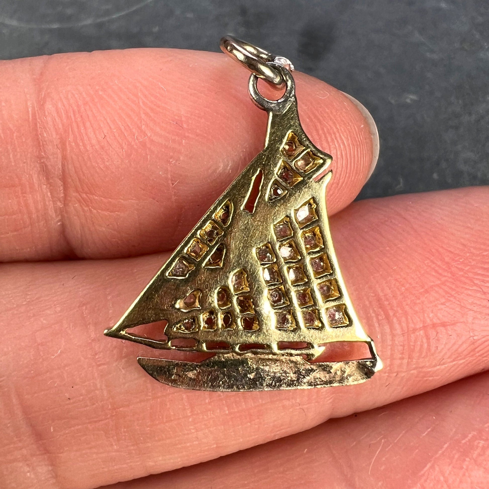 A diamond set yacht boat pendant, held in a hand on a grey background