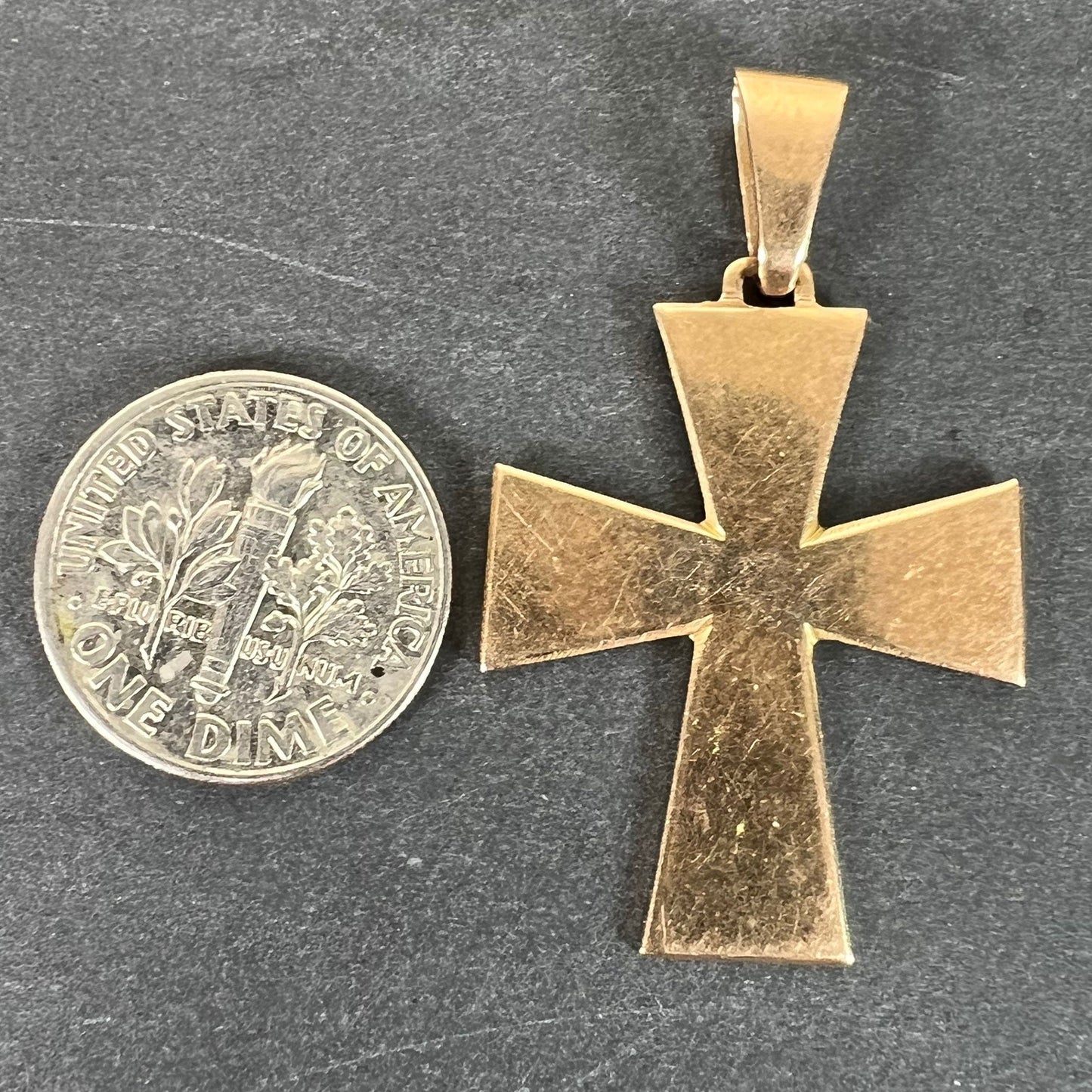 A plain gold cross pendant, next to a dime coin on a grey background