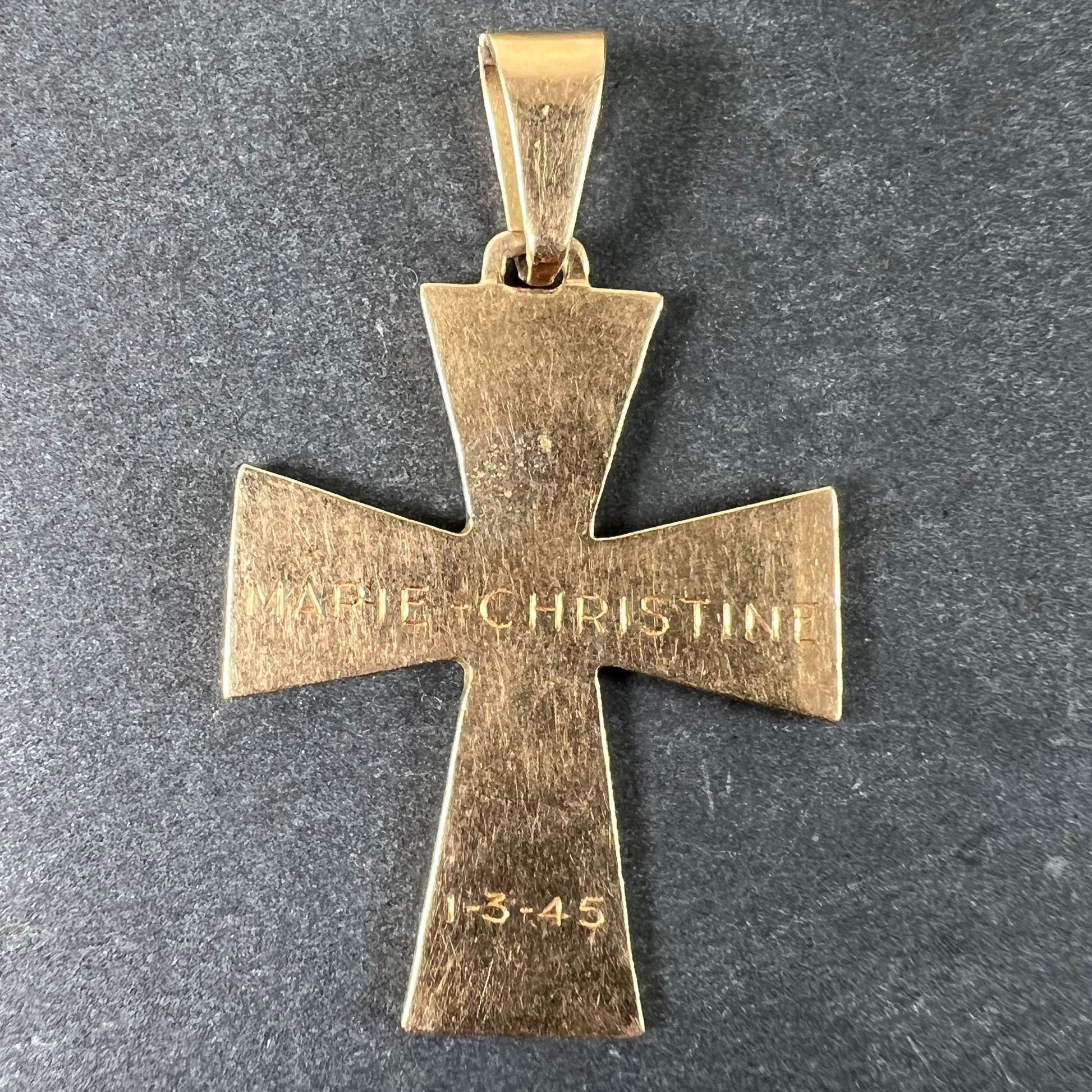 A plain gold cross pendant, engraved MARIE CHRISTINE 1-3-45, on a grey background