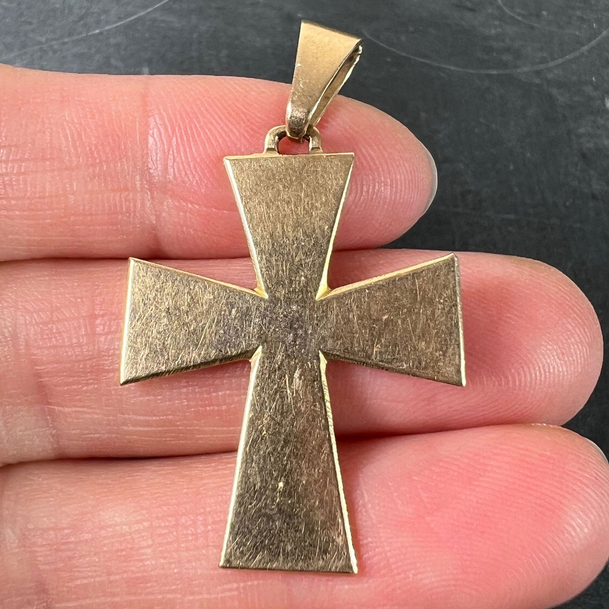 A plain gold cross pendant, held in a hand on a grey background