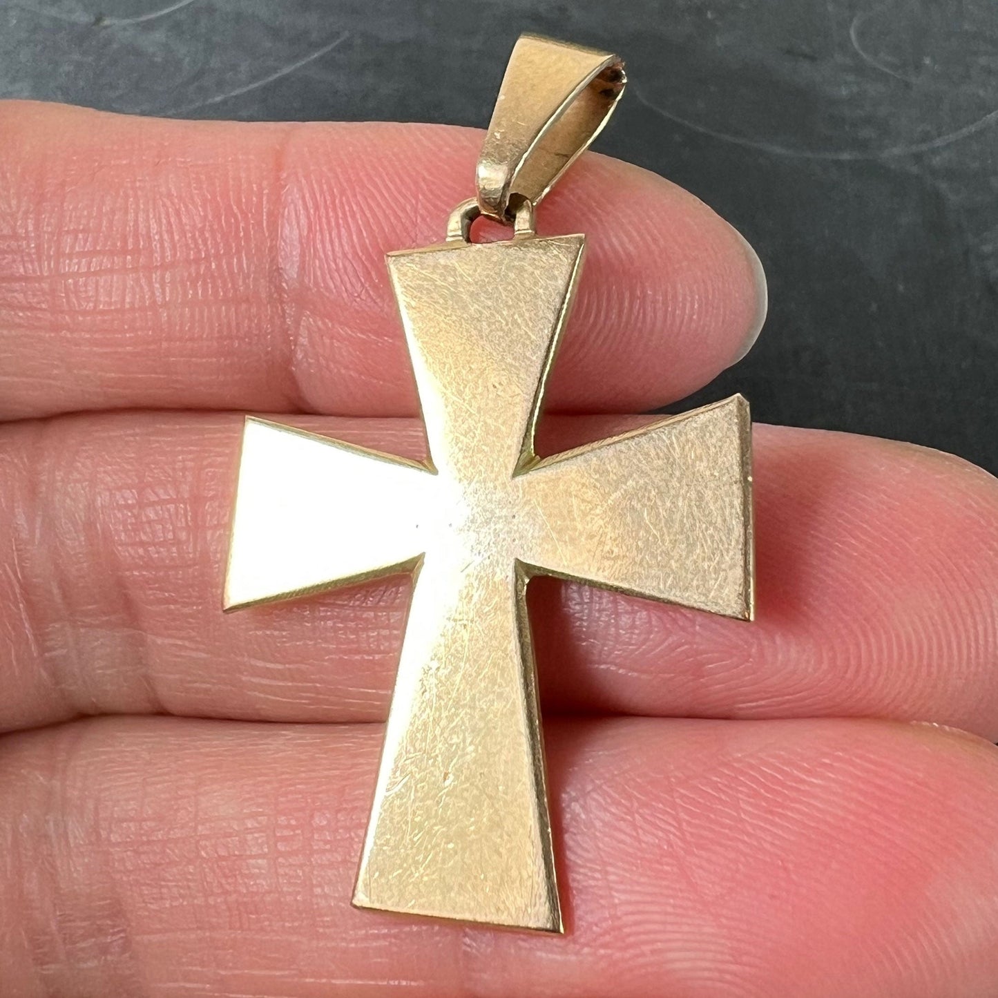 A plain gold cross pendant, held in a hand on a grey background