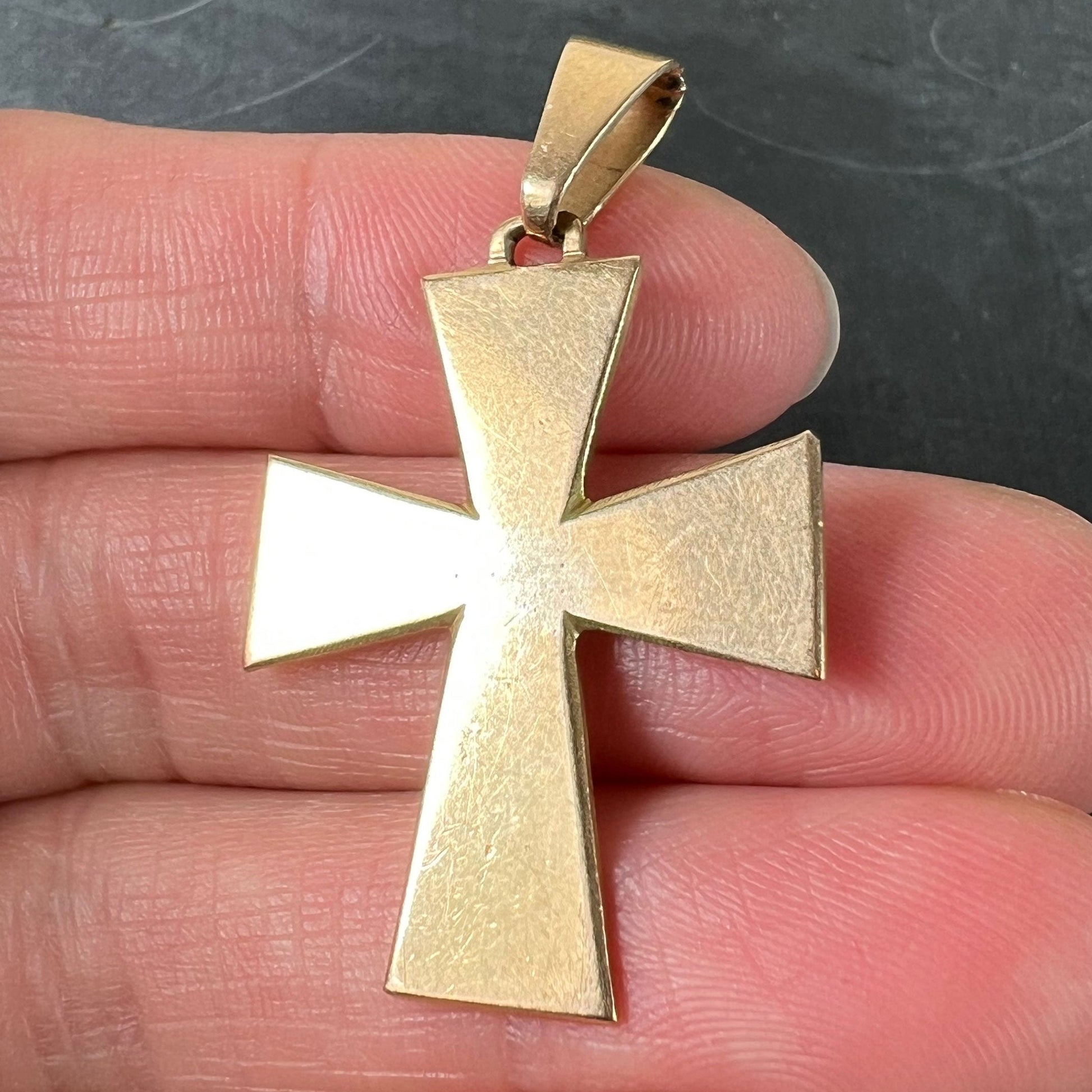 A plain gold cross pendant, held in a hand on a grey background