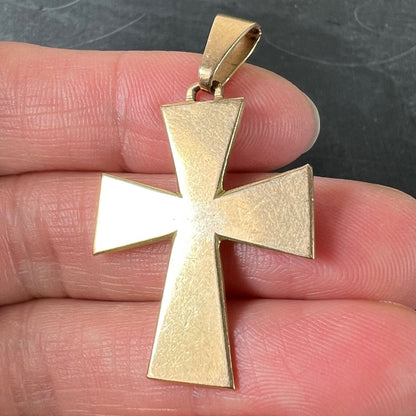 A plain gold cross pendant, held in a hand on a grey background
