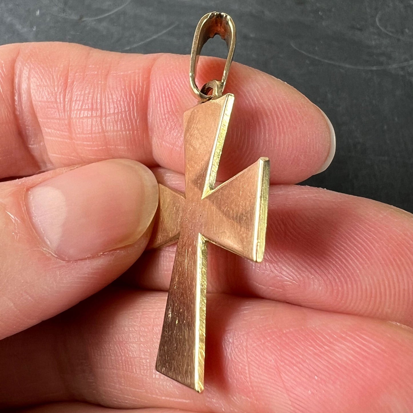 A plain gold cross pendant, held in a hand on a grey background