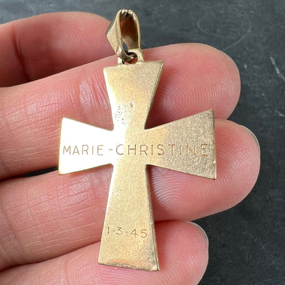 A plain gold cross pendant, engraved MARIE-CHRISTINE 1-3-45, held in a hand on a grey background