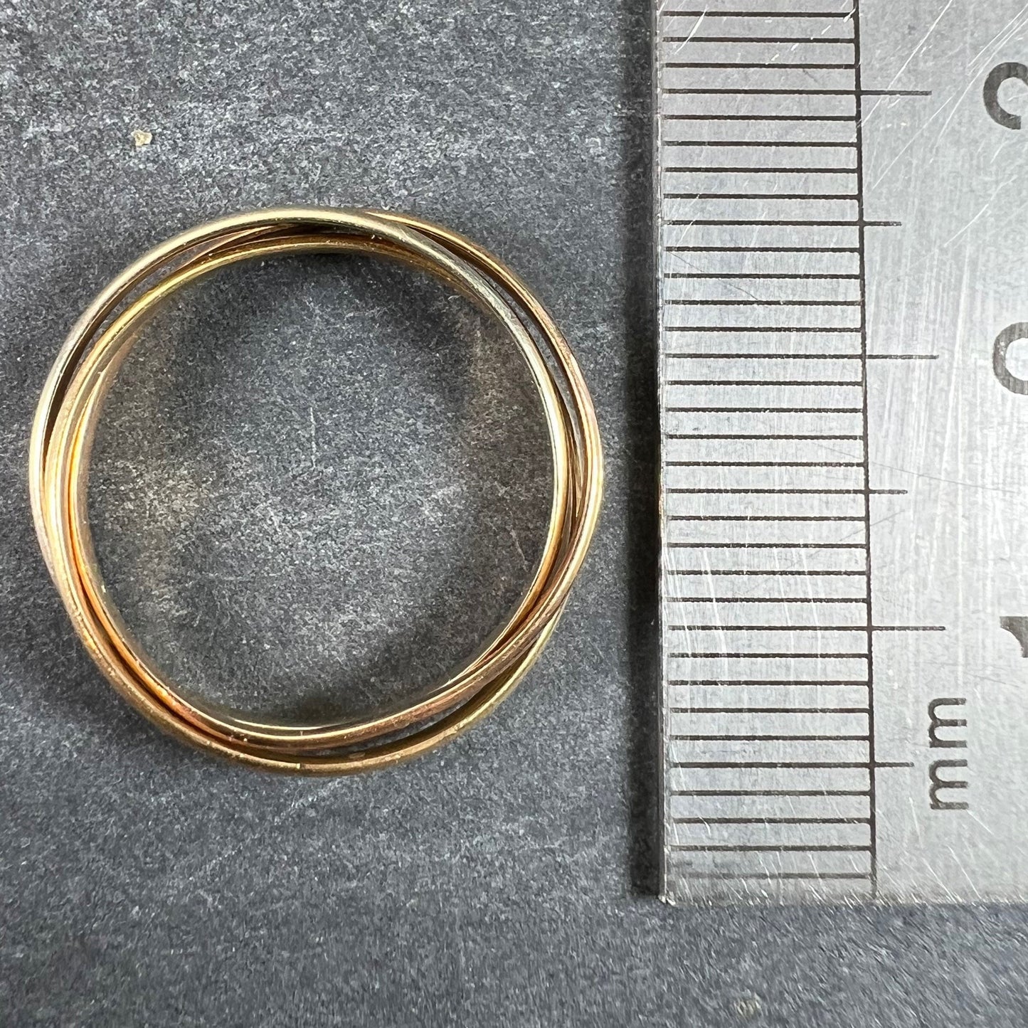 A tri-colour gold Russian wedding ring, next to a metal ruler on a grey background