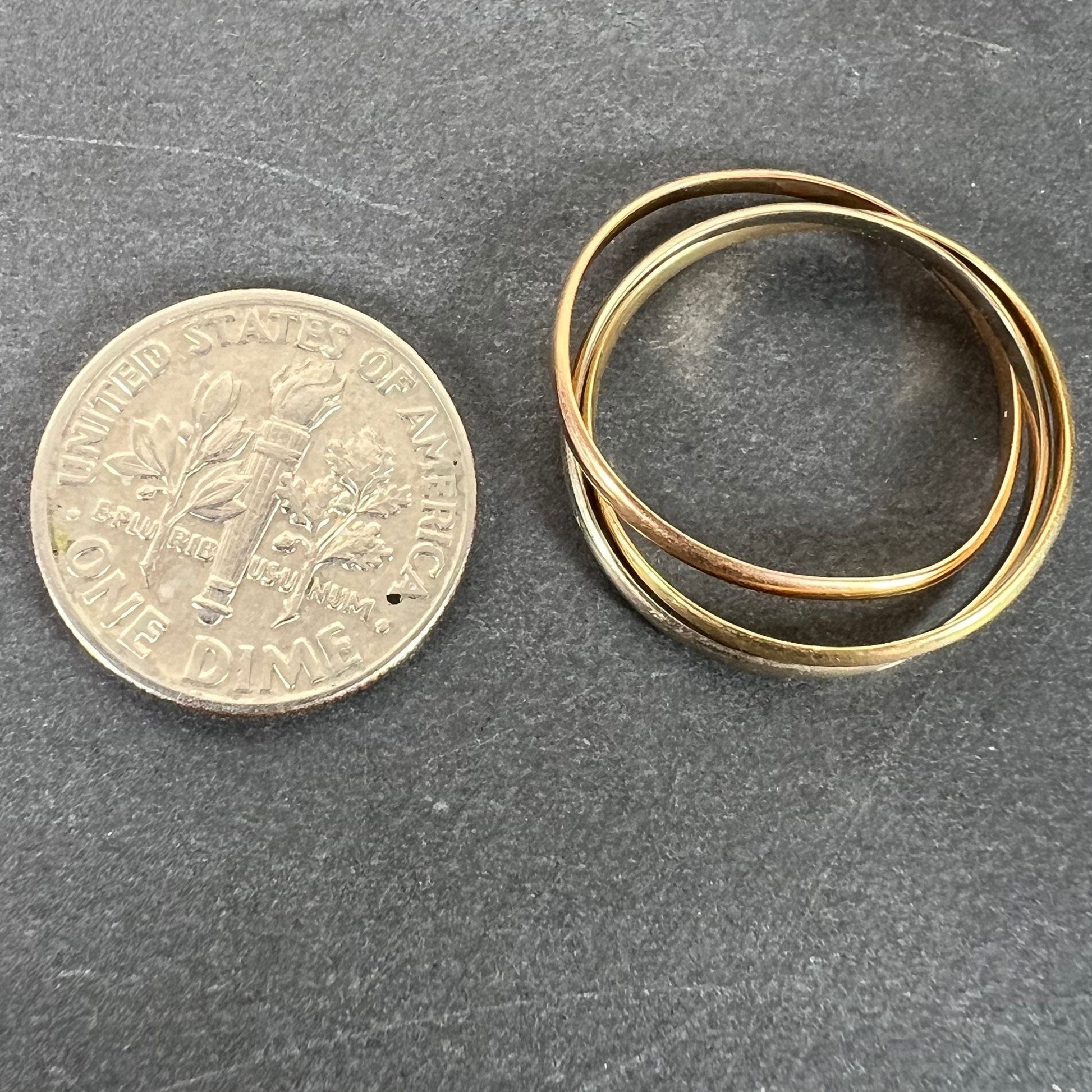 A tri-colour gold Russian wedding ring, next to a dime coin on a grey background