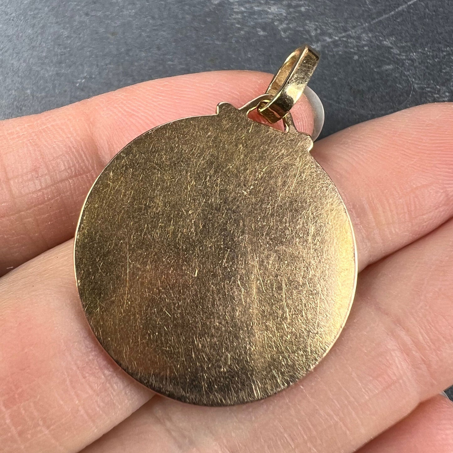 A round yellow gold pendant, held in a hand on a grey background
