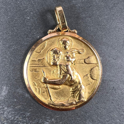 A round yellow gold Saint Christopher pendant, on a grey background