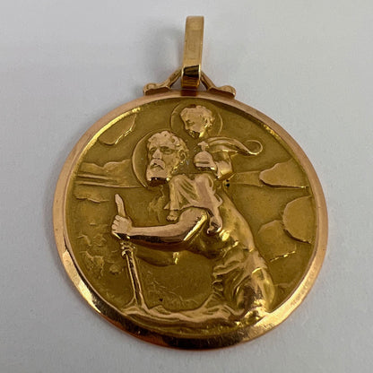 A round yellow gold Saint Christopher pendant, on a white background