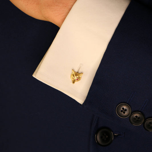 A fox head cufflink in yellow gold with ruby eyes, on a white shirt cuff against a dark blue suit