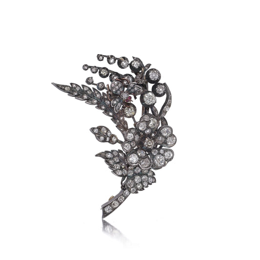 A decorative floral brooch set with old cut diamonds, in silver and gold, on a white background