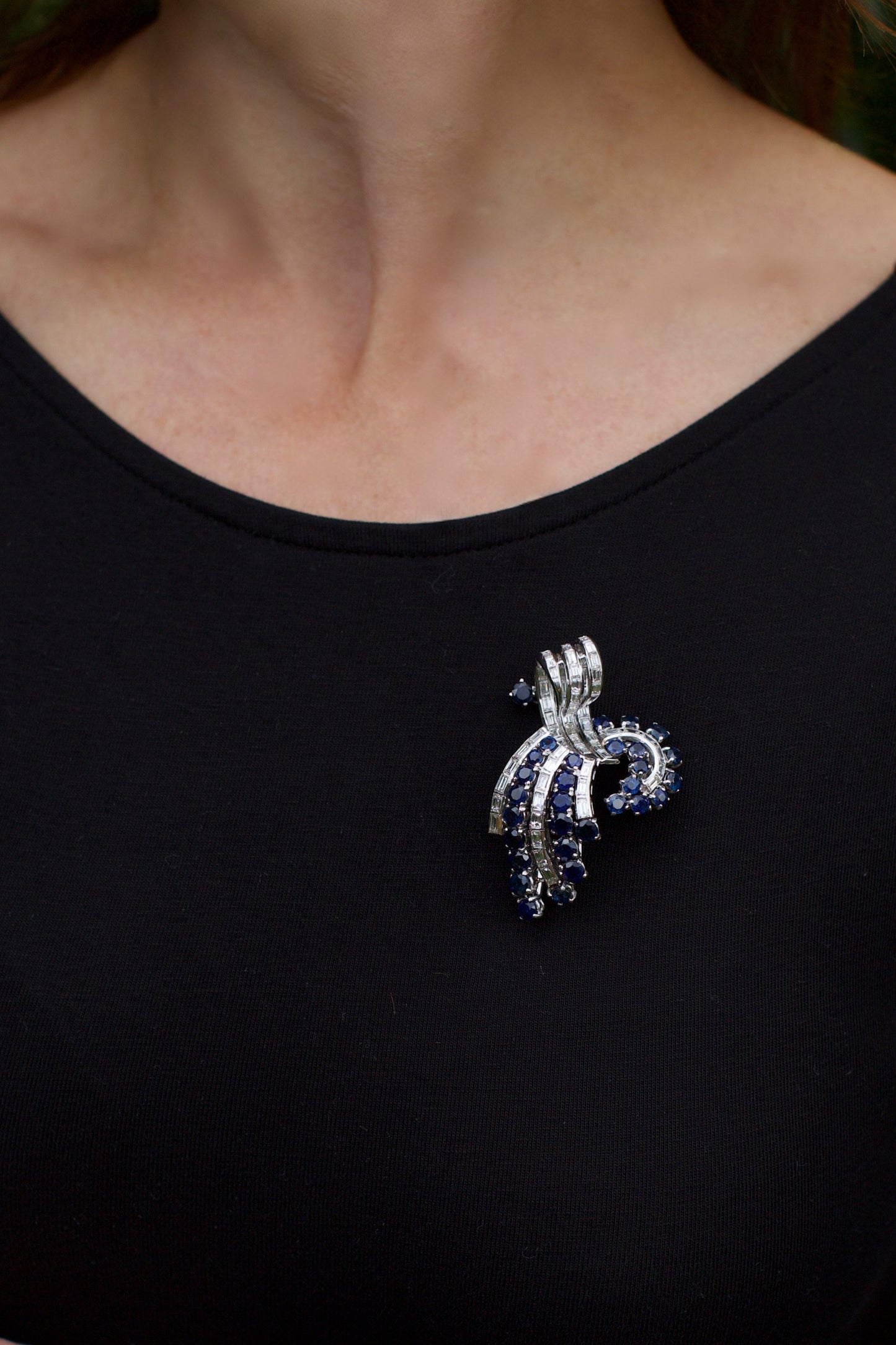 A decorative baguette cut diamond and round sapphire brooch in white metal, modelled on a lady wearing a black top