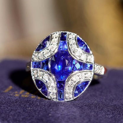 1.10ct Oval Sapphire and Diamond Geometric Cluster Dress Ring, 1.10ct oval-cut sapphire adorned by 1.25cts French cut sapphires with round brilliant diamond lines on each corner in 18ct white gold with millegrain edging