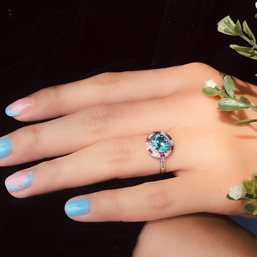 2.75ct Blue Zircon Ring with Ruby and Diamond Halo Cluster, central round-cut blue zircon is surrounded by rubies with a deep pink hue and diamonds with diamond-set shoulders in 14ct white gold