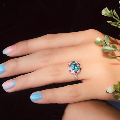 2.75ct Blue Zircon Ring with Ruby and Diamond Halo Cluster, central round-cut blue zircon is surrounded by rubies with a deep pink hue and diamonds with diamond-set shoulders in 14ct white gold