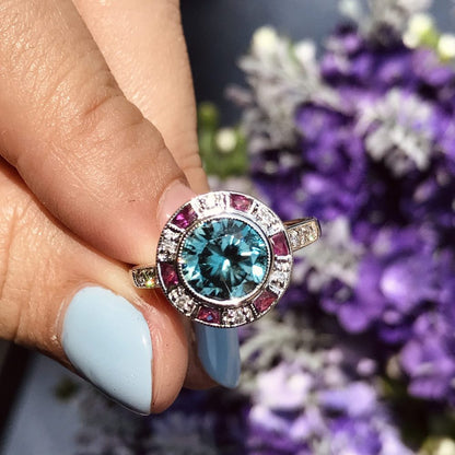 2.75ct Blue Zircon Ring with Ruby and Diamond Halo Cluster, central round-cut blue zircon is surrounded by rubies with a deep pink hue and diamonds with diamond-set shoulders in 14ct white gold