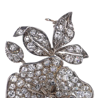 A decorative flower brooch set with diamonds, in silver and gold, on a white background