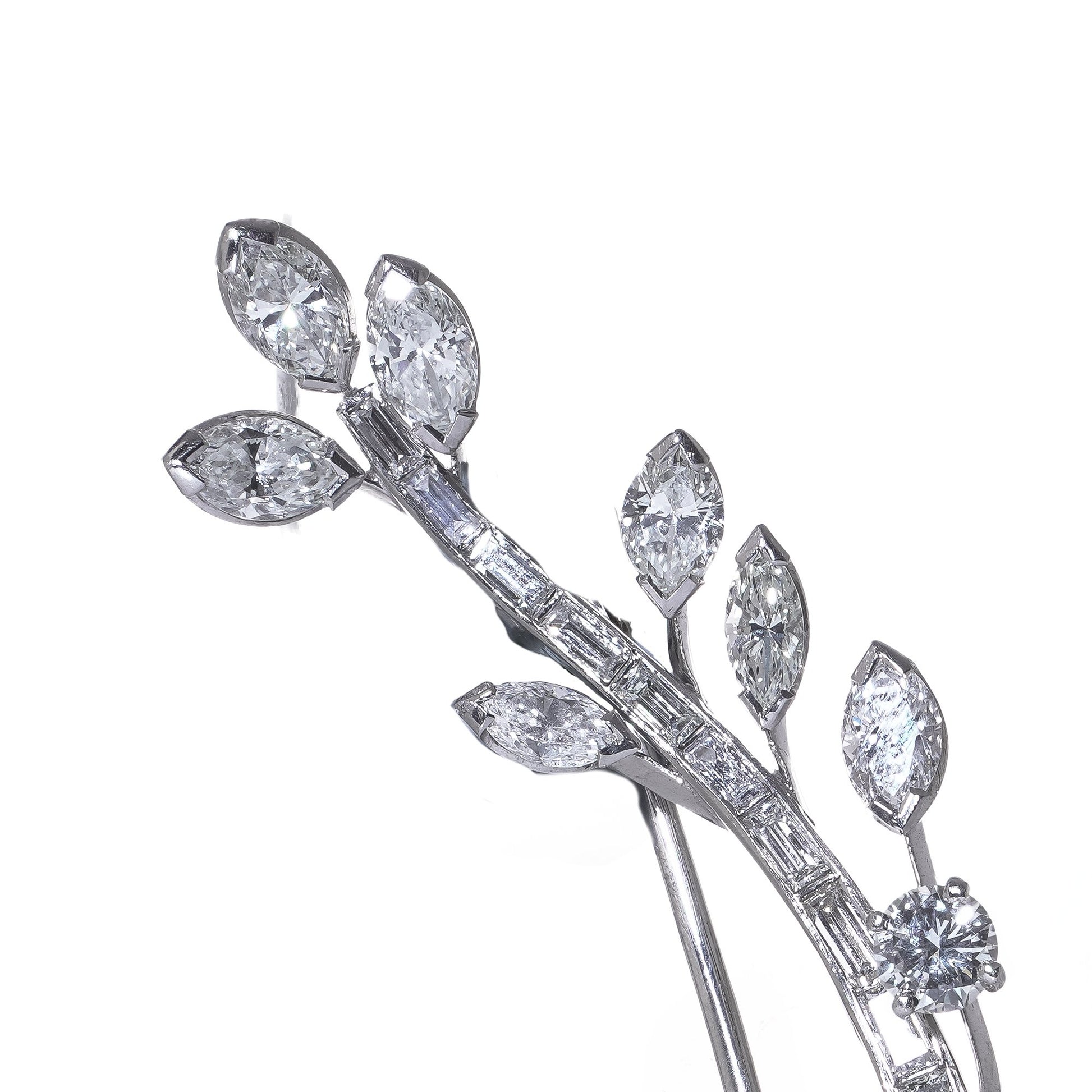 A leaf design brooch set with baguette, marquise and brilliant cut diamonds in white metal, on a white background