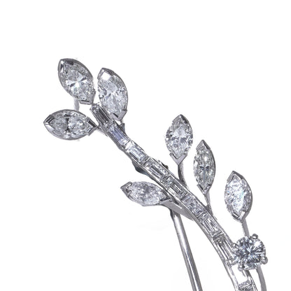 A leaf design brooch set with baguette, marquise and brilliant cut diamonds in white metal, on a white background