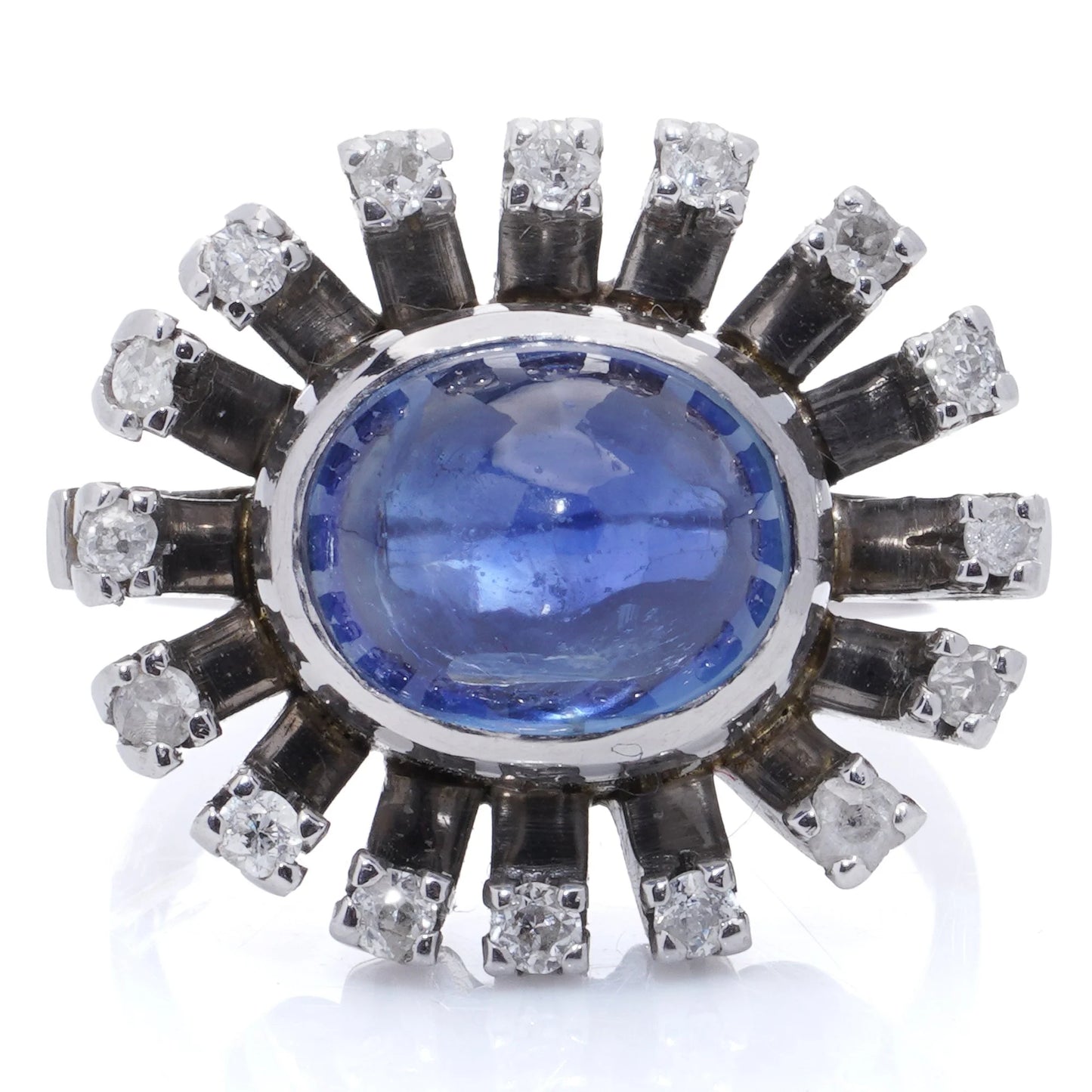 A cabochon blue sapphire and diamond ring in platinum, on a white background