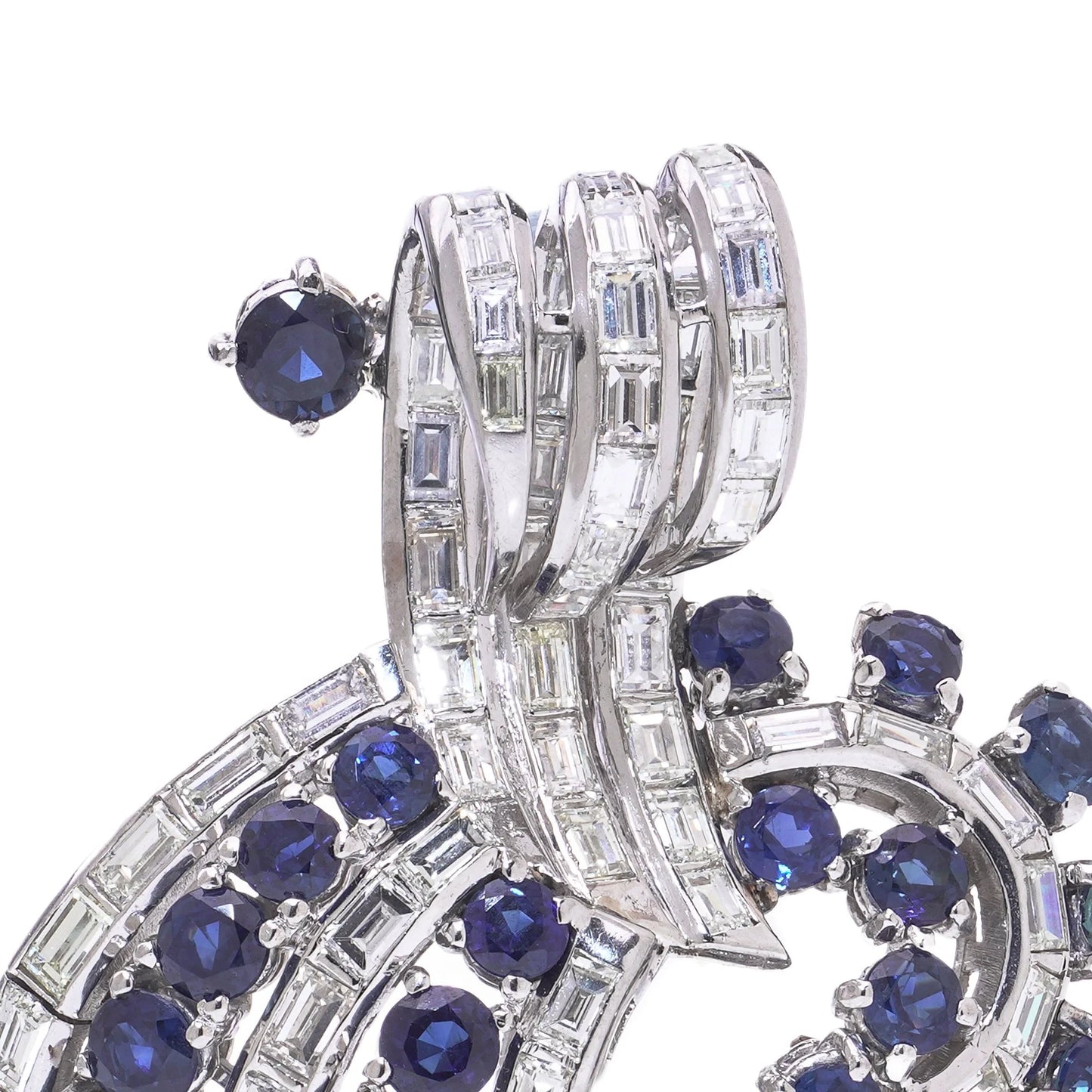 A decorative baguette cut diamond and round sapphire brooch in white metal, on a white background