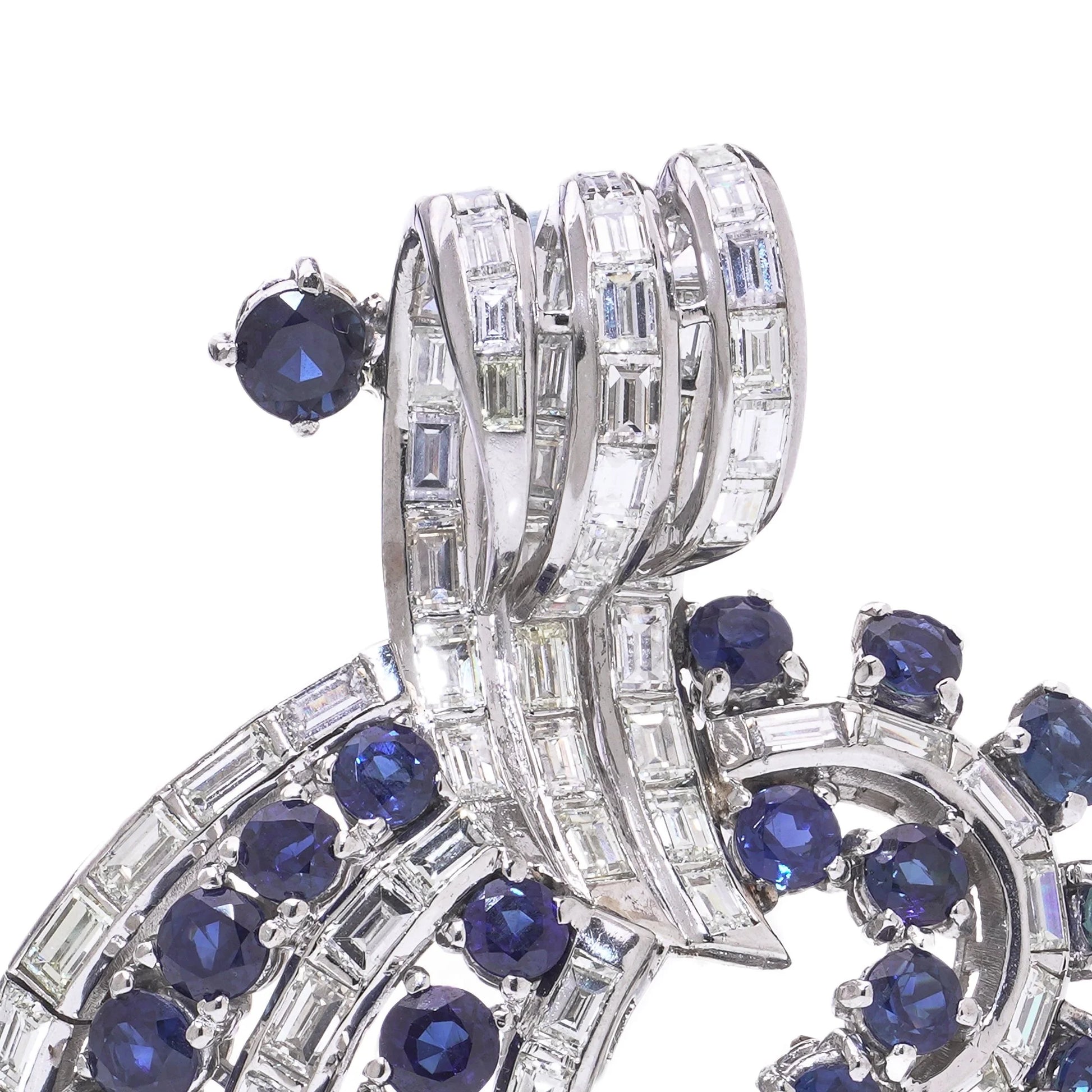 A decorative baguette cut diamond and round sapphire brooch in white metal, on a white background