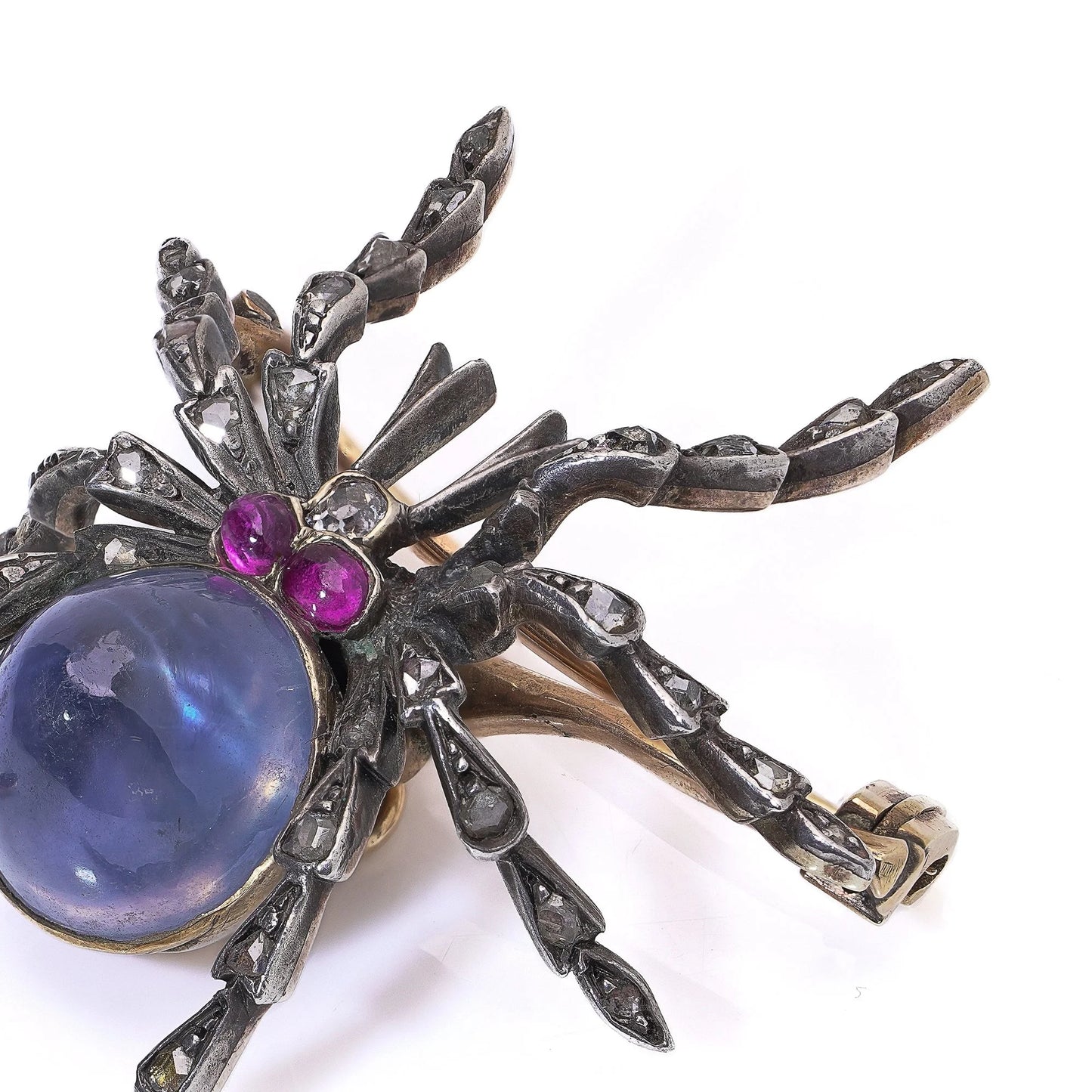 A spider brooch with a sapphire and ruby body and diamond legs, in silver and gold, on a white background