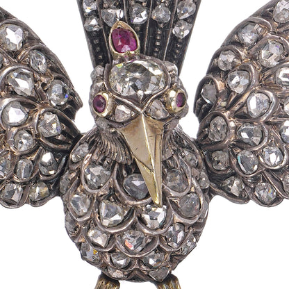 An antique bird in flight brooch set with diamonds and rubies, in silver and gold, on a white background